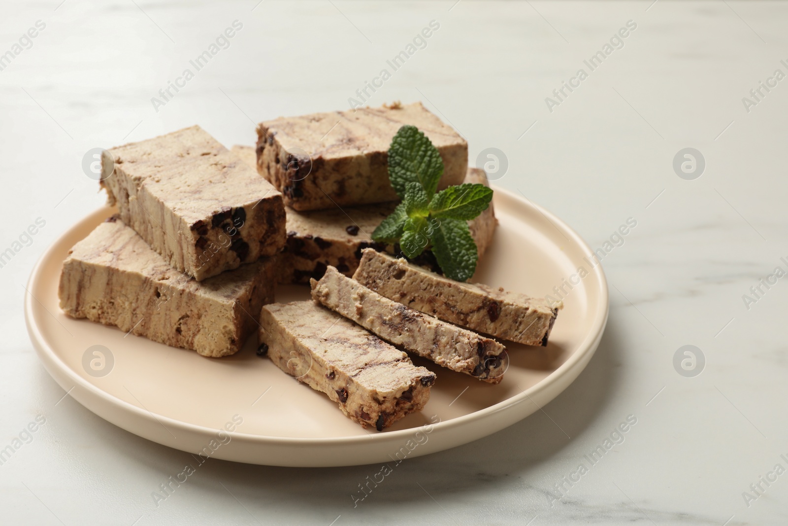 Photo of Pieces of tasty chocolate halva and mint on white marble table, space for text