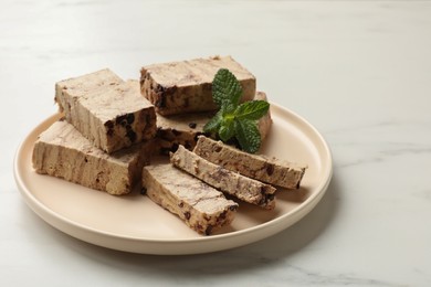 Photo of Pieces of tasty chocolate halva and mint on white marble table, space for text