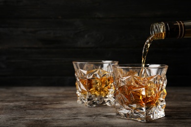 Photo of Pouring whiskey from bottle in to glass with ice cubes on table. Space for text