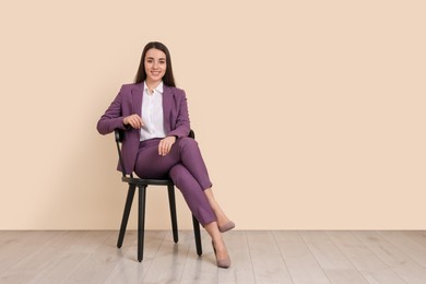 Photo of Young businesswoman sitting on chair near beige wall in office, space for text