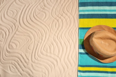 Photo of Bright towel and hat on sand, top view with space for text. Beach objects