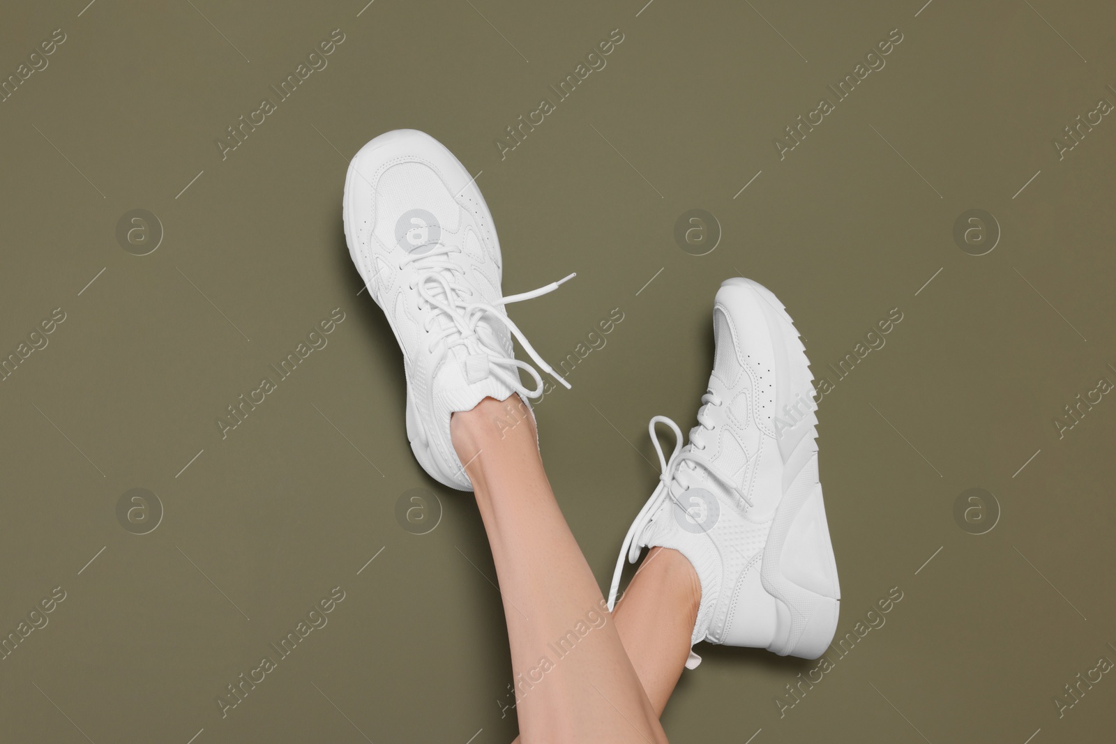 Photo of Woman wearing pair of new stylish sneakers on dark olive background, closeup