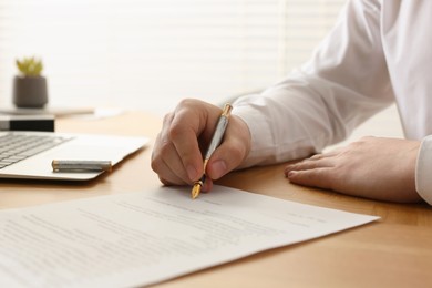 Photo of Notary signing document at wooden table indoors, closeup