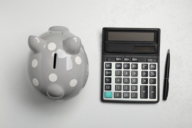 Calculator, pen and piggy bank on white table, flat lay