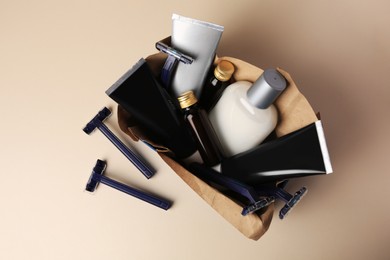 Photo of Box with different men's shaving accessories and cosmetics on beige background, flat lay