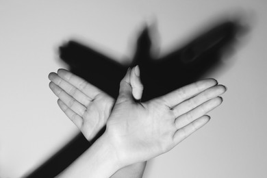Photo of Shadow puppet. Woman making hand gesture like bird on light background, closeup. Black and white effect