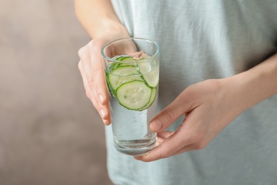 Photo of Young woman holding glass with fresh cucumber water, closeup. Space for text