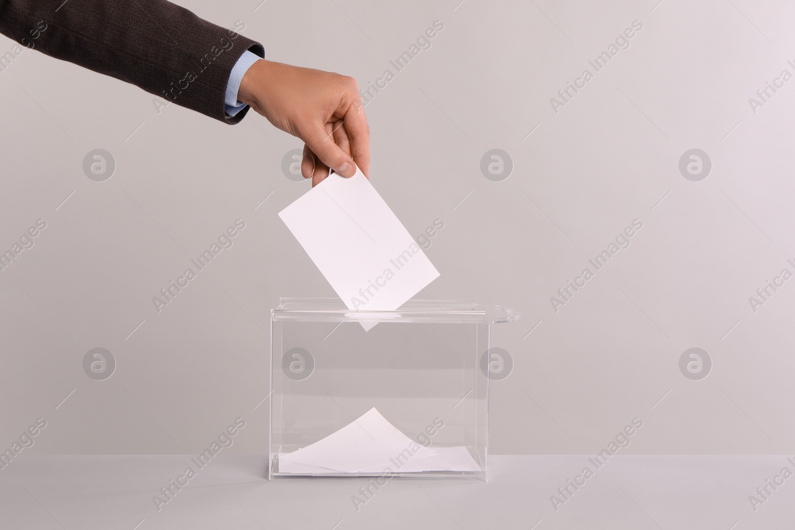 Photo of Man putting his vote into ballot box on light grey background, closeup. Space for text