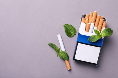 Photo of Pack of menthol cigarettes and mint leaves on grey background, flat lay. Space for text