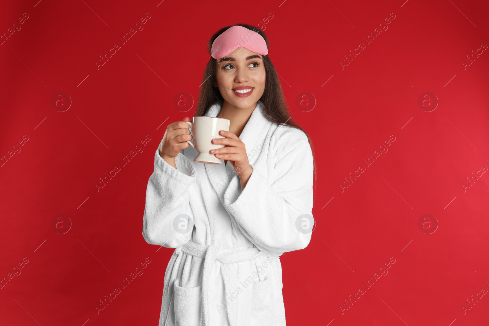 Photo of Young woman in bathrobe with cup of coffee on red background