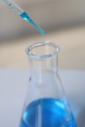 Laboratory analysis. Dripping blue liquid into flask on table, closeup