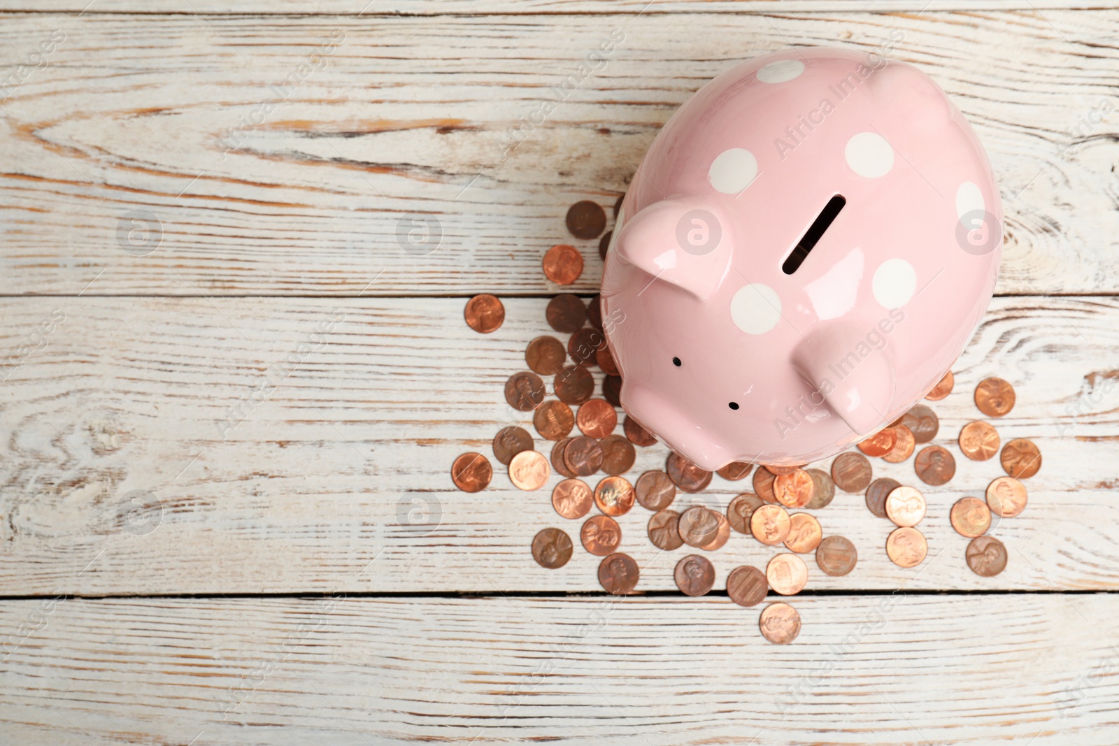 Photo of Ceramic piggy bank, many coins and space for text on white wooden background, top view