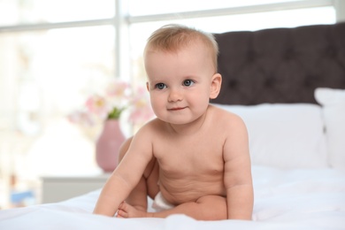 Cute baby in diaper on bed at home