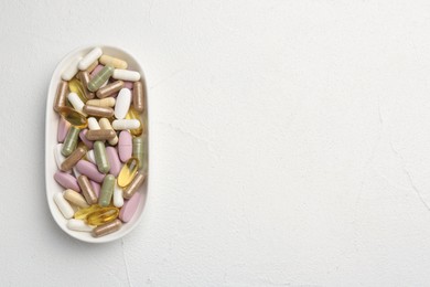 Different vitamin capsules in bowl on white wooden table, top view. Space for text