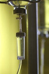 Photo of IV drip chamber against blurred yellow background