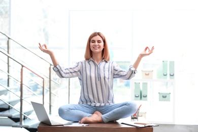 Beautiful woman meditating on table in office during break. Zen yoga