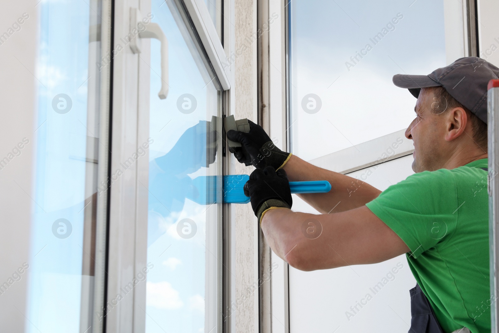 Photo of Worker in uniform using spatula for window installation indoors