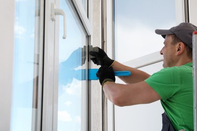 Worker in uniform using spatula for window installation indoors