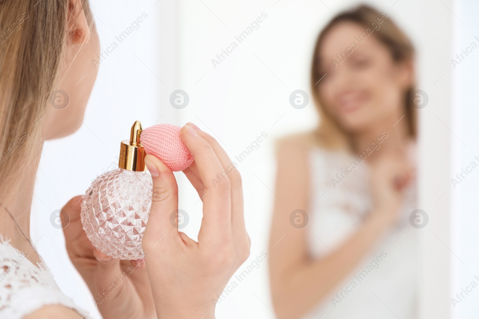 Photo of Beautiful young bride with bottle of perfume near mirror indoors, space for text
