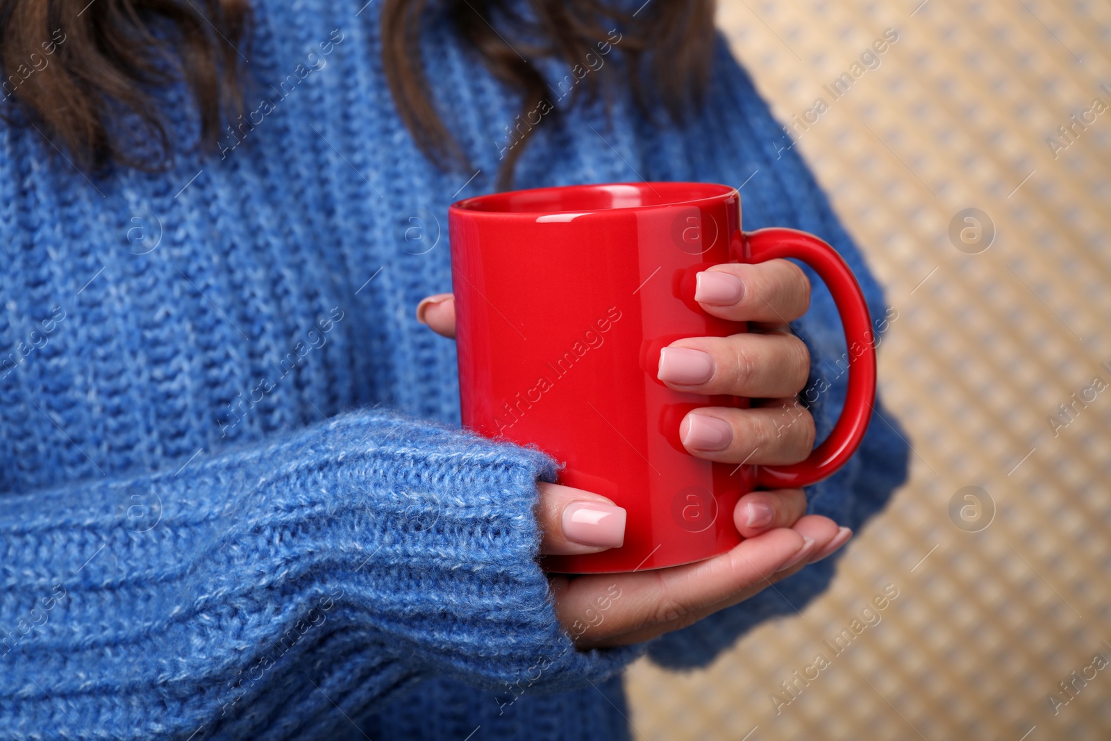 Photo of Woman holding red mug on beige background, closeup. Mockup for design