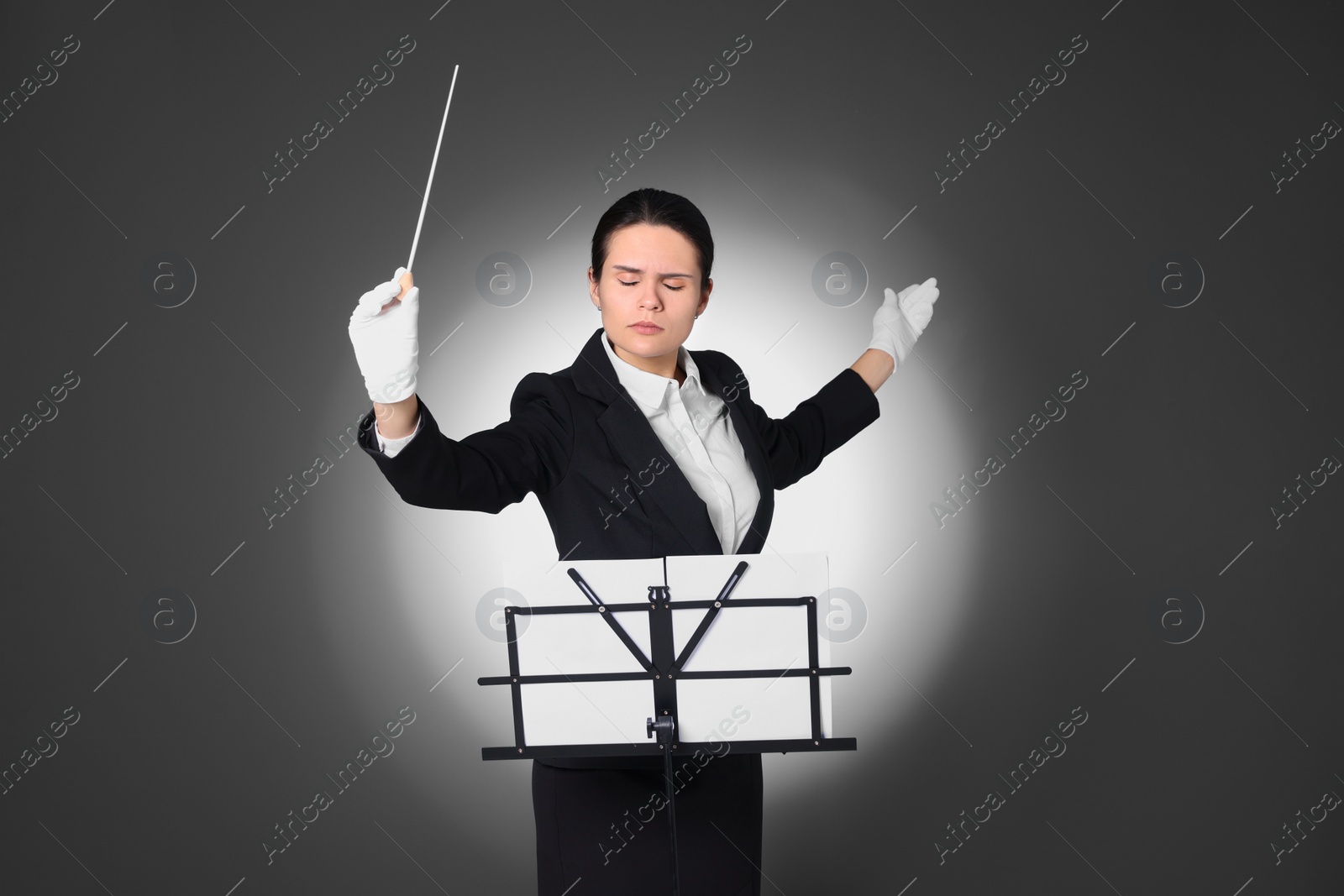 Photo of Professional conductor with baton and note stand on grey background