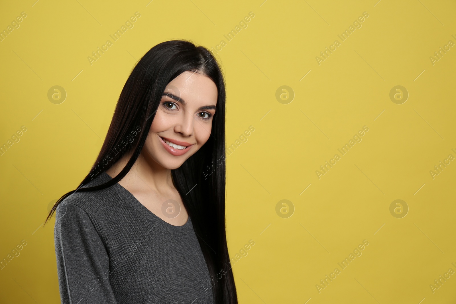 Photo of Portrait of happy young woman with beautiful black hair and charming smile on yellow background, space for text