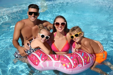 Happy family with inflatable ring in outdoor swimming pool on sunny summer day