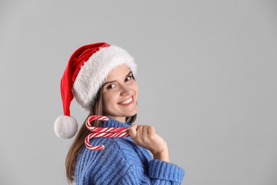 Photo of Pretty woman in Santa hat and blue sweater holding candy canes on grey background, space for text
