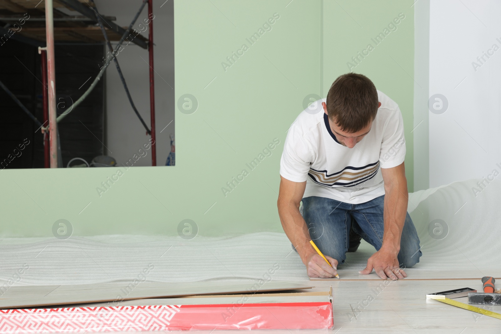 Photo of Man using pencil during installation of new laminate flooring in room