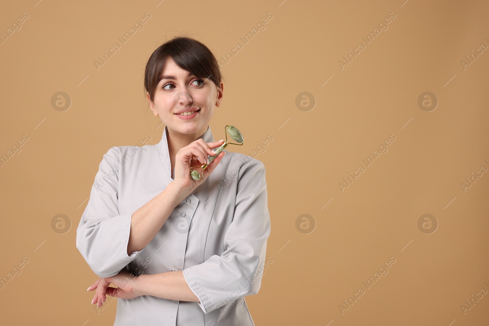Photo of Cosmetologist with facial roller on beige background, space for text