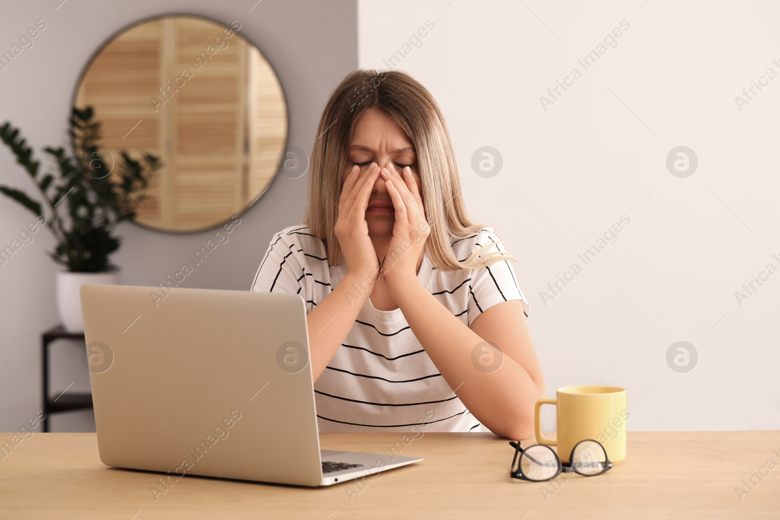 Photo of Sleepy young woman with laptop at wooden table indoors