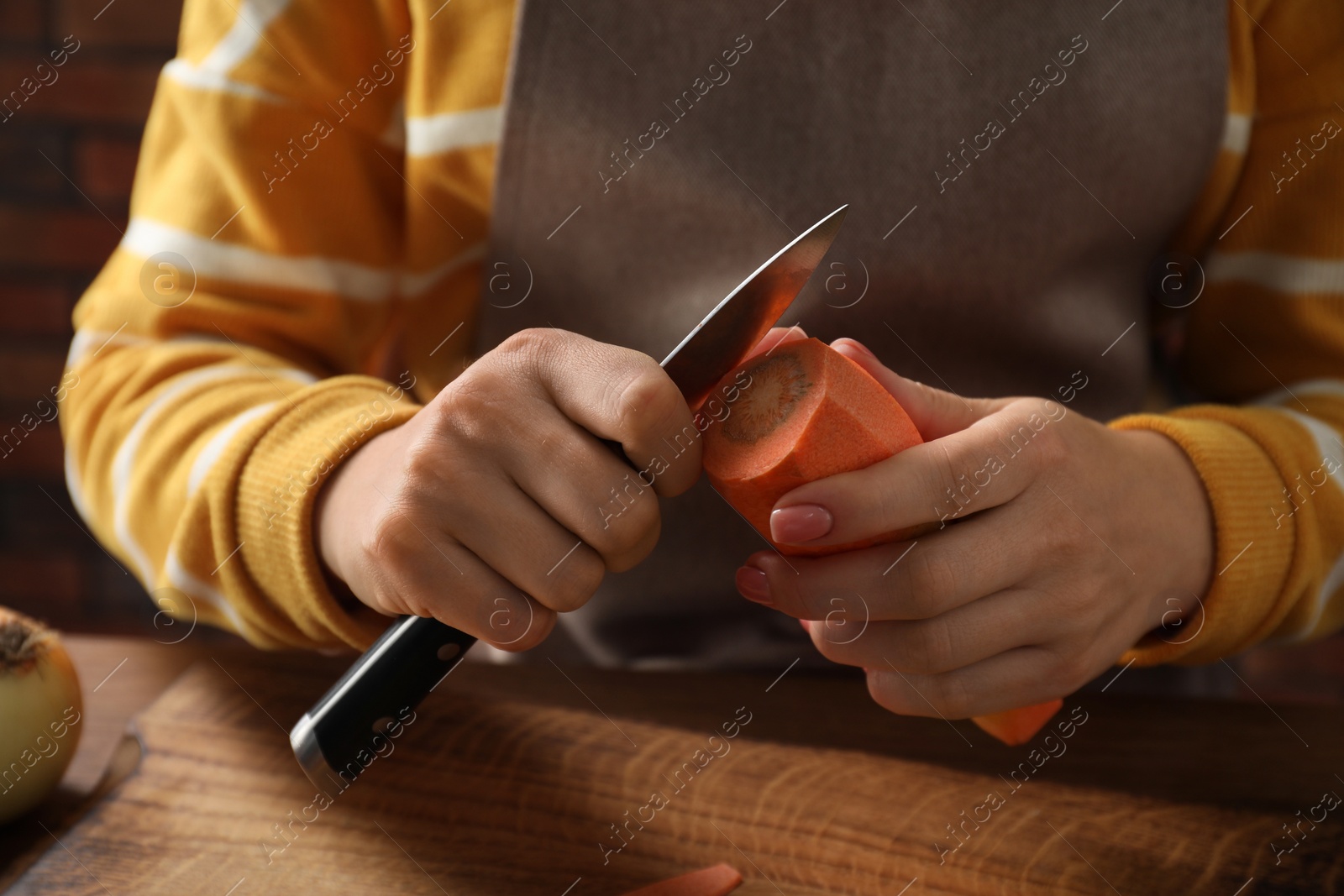 Photo of Woman peeling fresh carrot with knife at wooden table indoors, closeup