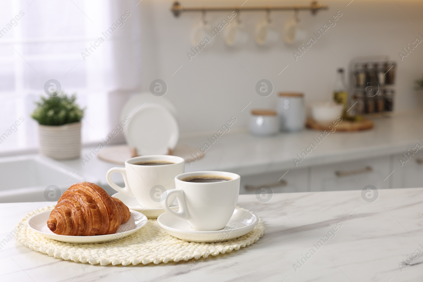 Photo of Breakfast served in kitchen. Cups of coffee and fresh croissant on white marble table. Space for text