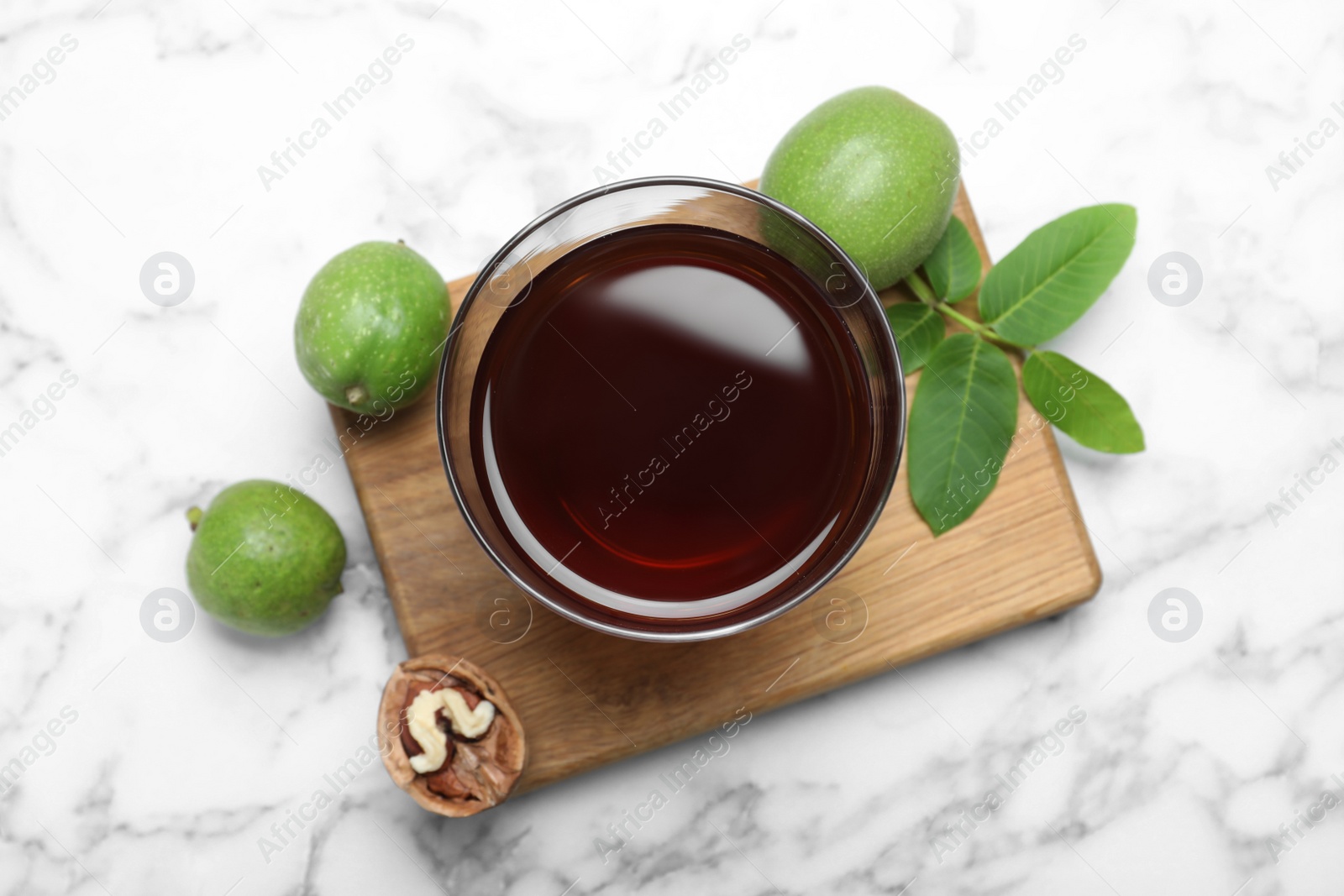 Photo of Delicious liqueur and fresh walnuts on white marble table, flat lay