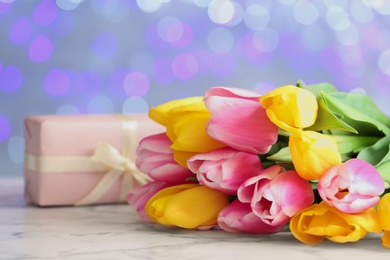 Photo of Bouquet of flowers and gift box on table against blurred lights, space for text