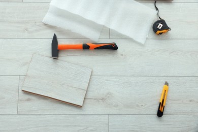 Photo of Hammer, cutter knife and measuring tape on laminated floor, flat lay