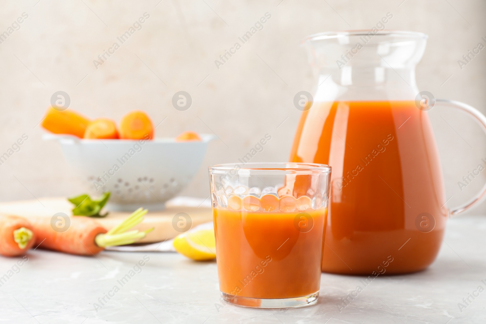 Photo of Glass and jug of carrot drink on light table, space for text