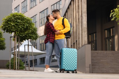 Photo of Long-distance relationship. Beautiful couple with luggage kissing outdoors, low angle view