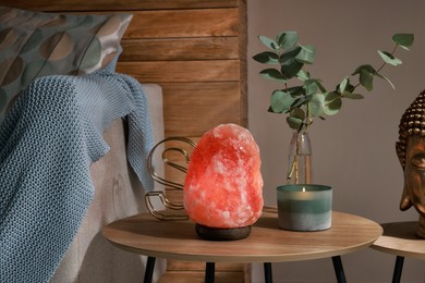 Photo of Beautiful Himalayan salt lamp, eucalyptus branches and candle on wooden table in living room