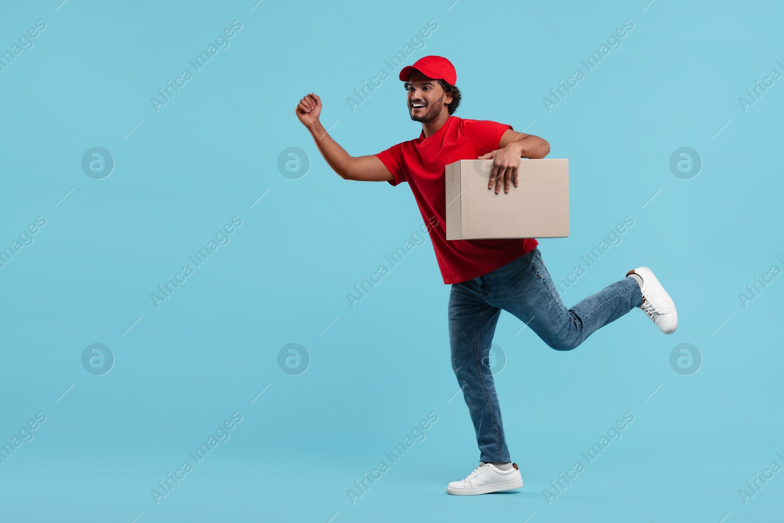 Photo of Happy young courier running to deliver parcel on light blue background, space for text