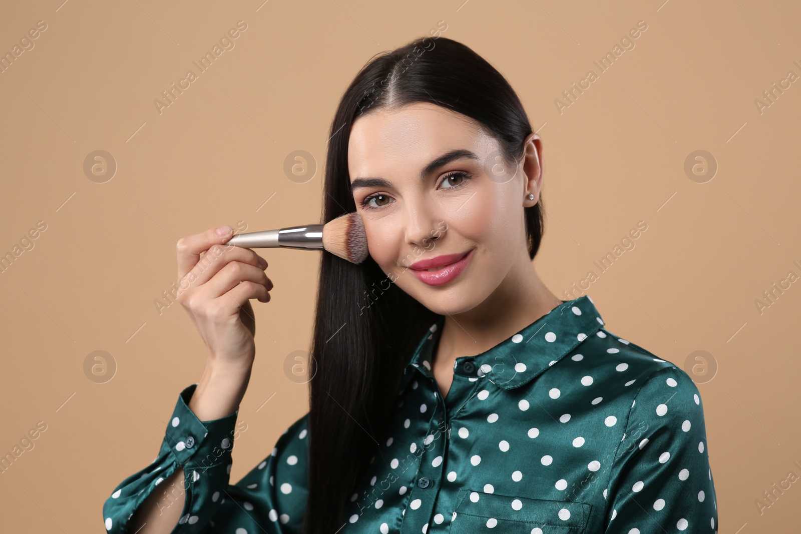 Photo of Beautiful woman applying makeup on light brown background