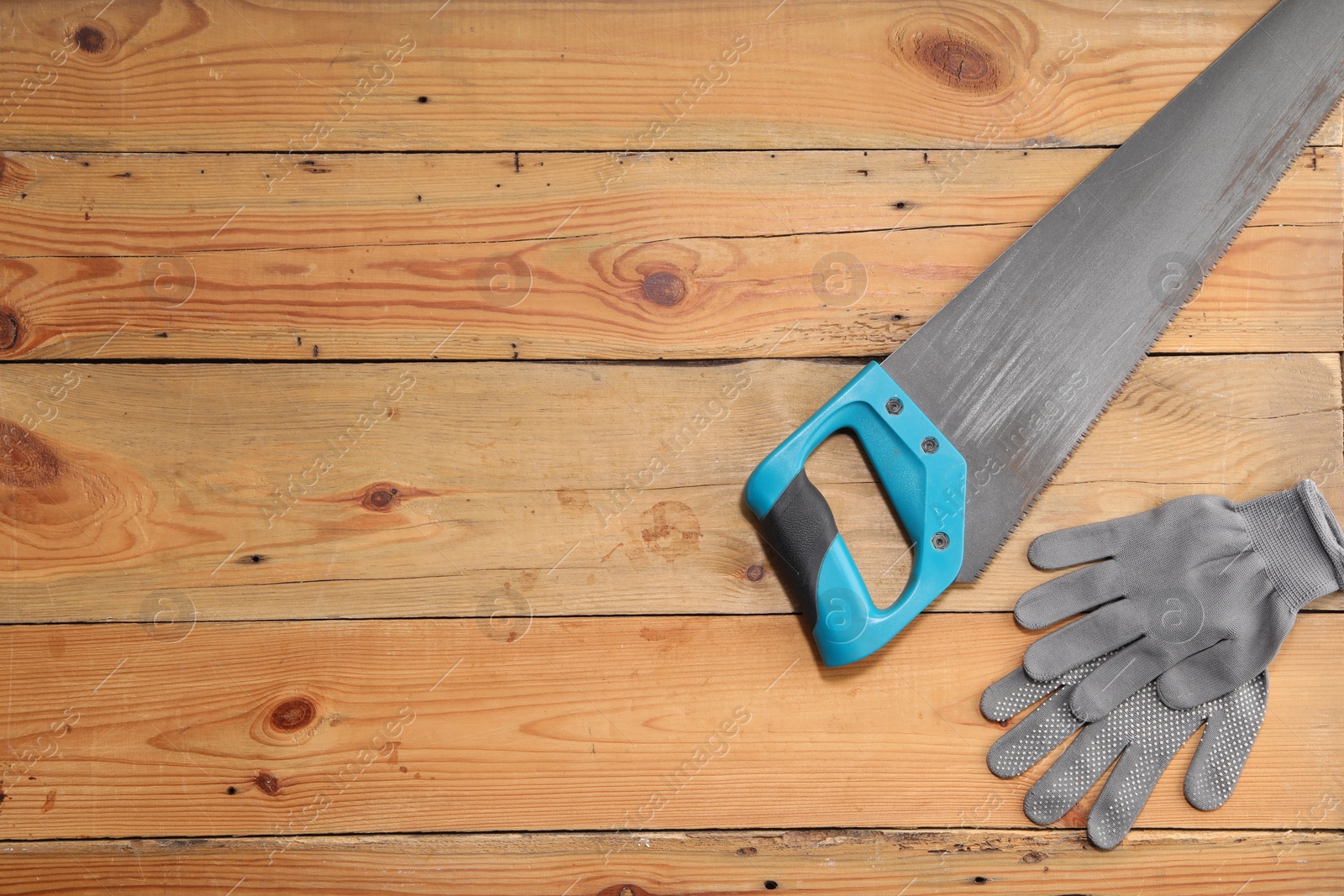 Photo of Saw with light blue handle and gloves on wooden background, flat lay. Space for text