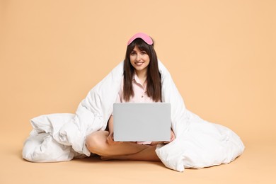 Happy woman with pyjama and blanket holding laptop on beige background