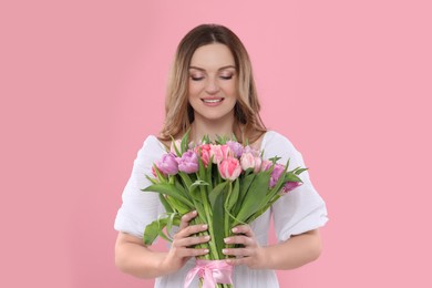 Happy young woman with bouquet of beautiful tulips on pink background