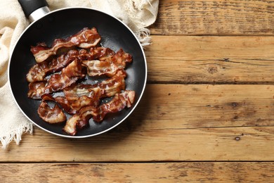 Photo of Delicious bacon slices in frying pan on wooden table, top view. Space for text