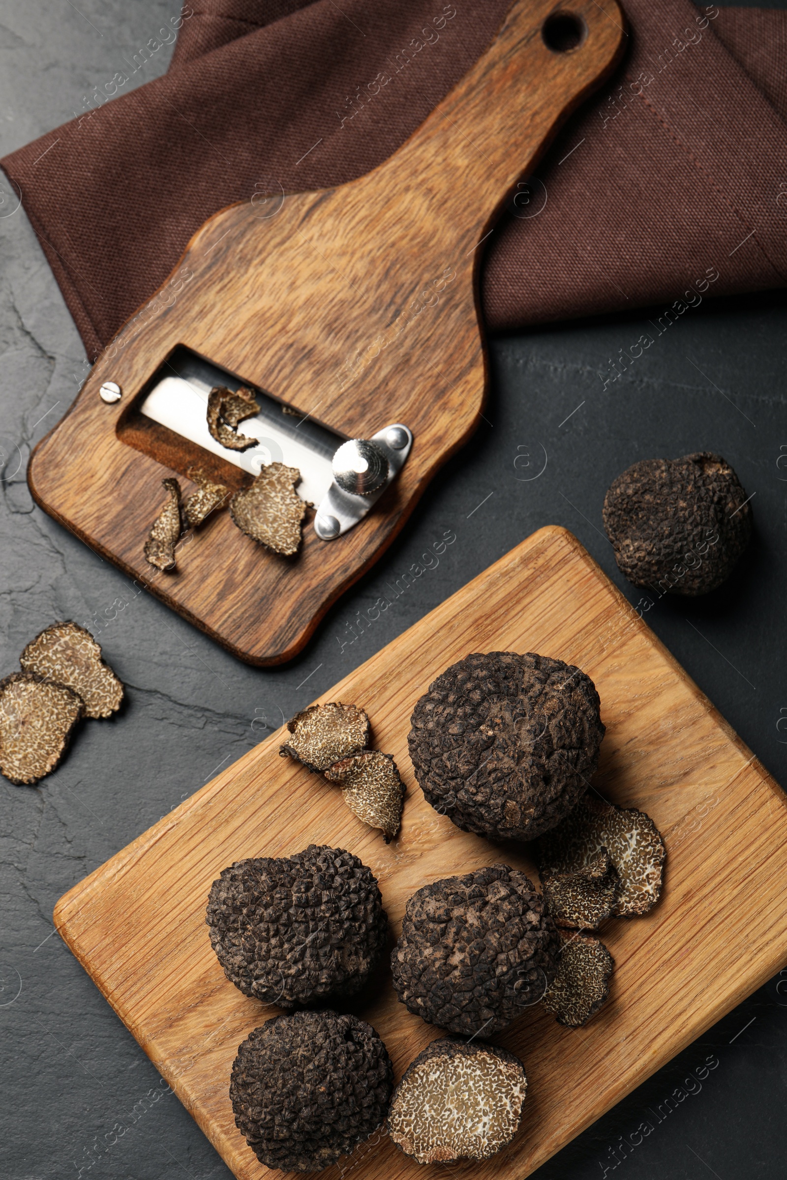 Photo of Wooden shaver with whole and sliced truffles on black table, flat lay