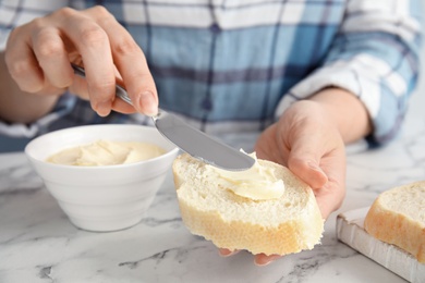 Photo of Woman spreading butter onto slice of bread over marble table, closeup