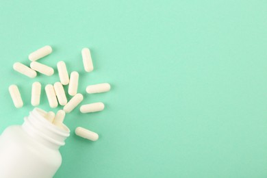 Photo of Bottle and vitamin capsules on turquoise background, top view. Space for text