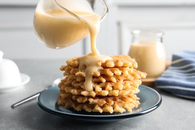 Photo of Pouring condensed milk from jug onto waffles on grey table. Dairy product