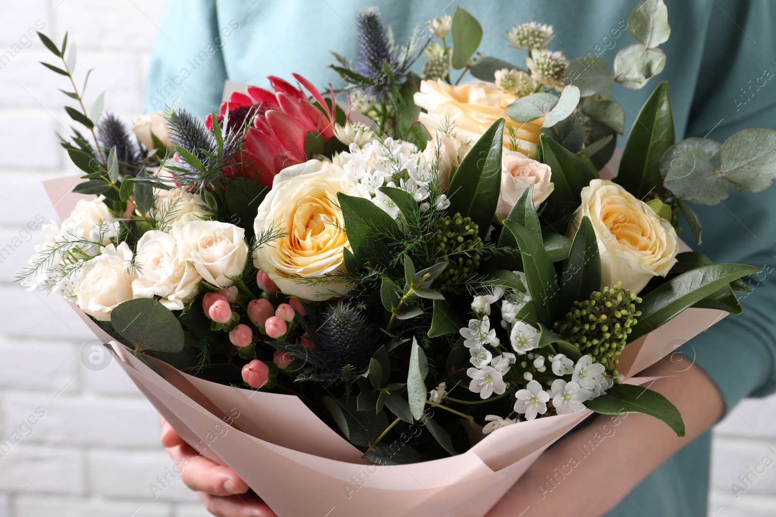 Photo of Woman with bouquet of beautiful roses near white brick wall, closeup